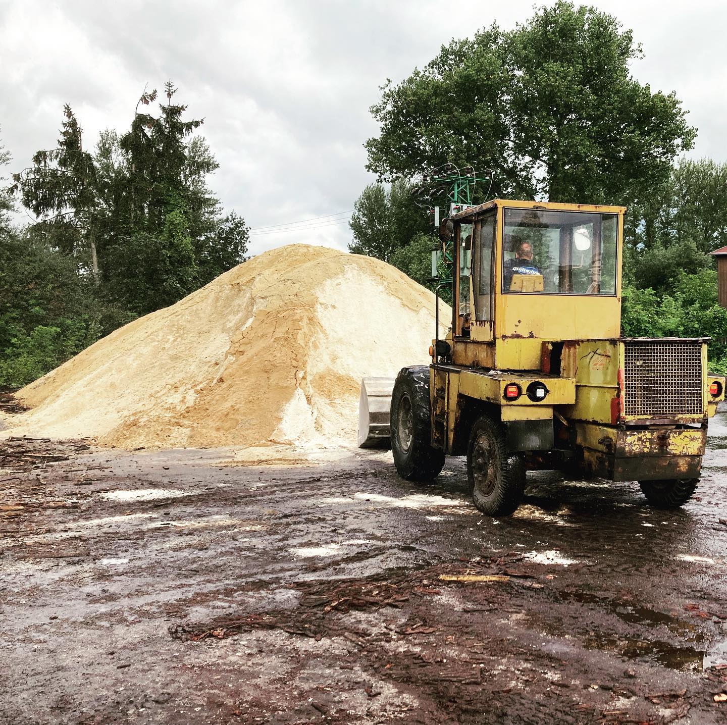 Žlutý nakladač u hromady pilin na vytápění